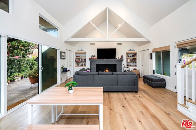 living room with built in features, a fireplace, high vaulted ceiling, and light hardwood / wood-style flooring