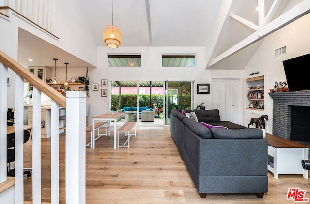 living room with built in features, a fireplace, high vaulted ceiling, and light hardwood / wood-style floors