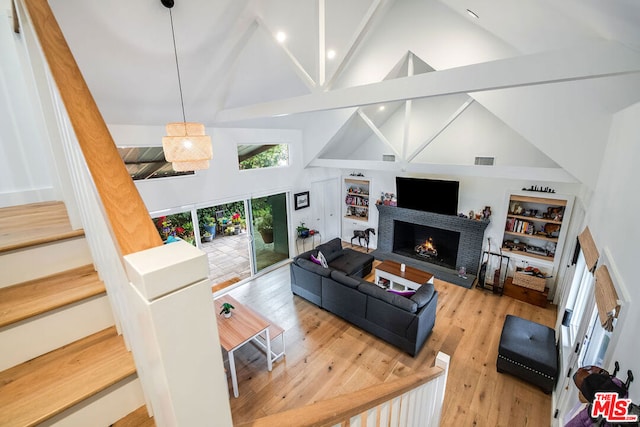 living room with high vaulted ceiling, a fireplace, light hardwood / wood-style floors, and built in shelves