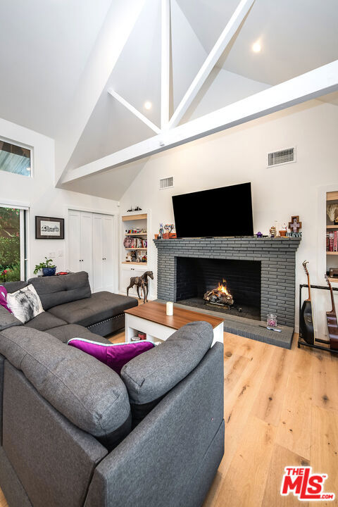 living room with wood-type flooring, high vaulted ceiling, and a fireplace