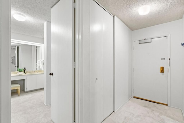 hallway featuring light colored carpet and a textured ceiling