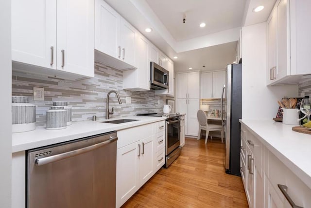 kitchen with sink, white cabinetry, light hardwood / wood-style flooring, appliances with stainless steel finishes, and backsplash