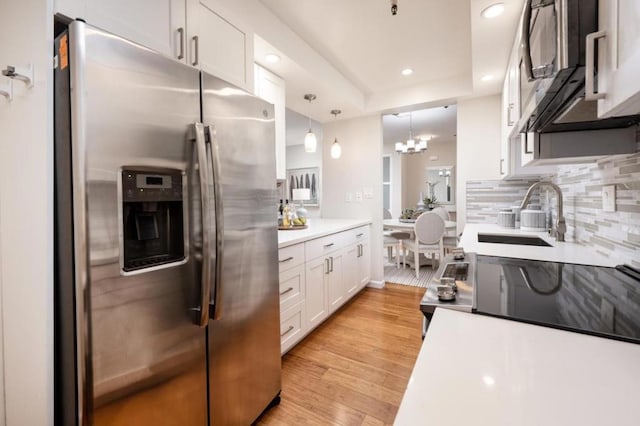 kitchen with appliances with stainless steel finishes, decorative light fixtures, sink, white cabinets, and light hardwood / wood-style floors