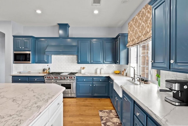 kitchen with built in microwave, sink, blue cabinets, and range with two ovens