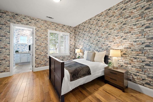 bedroom with ensuite bath and light hardwood / wood-style floors