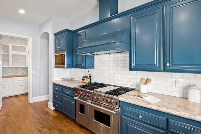 kitchen featuring premium range hood, dark hardwood / wood-style floors, blue cabinets, range with two ovens, and light stone countertops