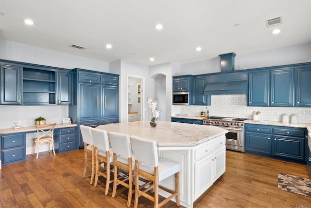 kitchen with blue cabinetry, appliances with stainless steel finishes, a center island, and built in desk