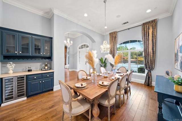 dining space with ornamental molding, beverage cooler, a chandelier, and light wood-type flooring