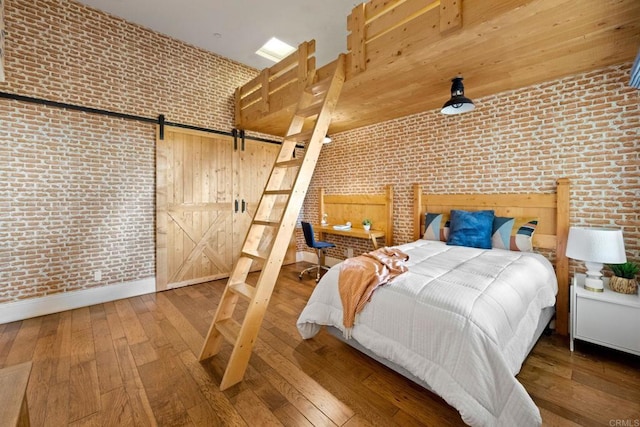 unfurnished bedroom featuring brick wall, a barn door, hardwood / wood-style flooring, and a towering ceiling