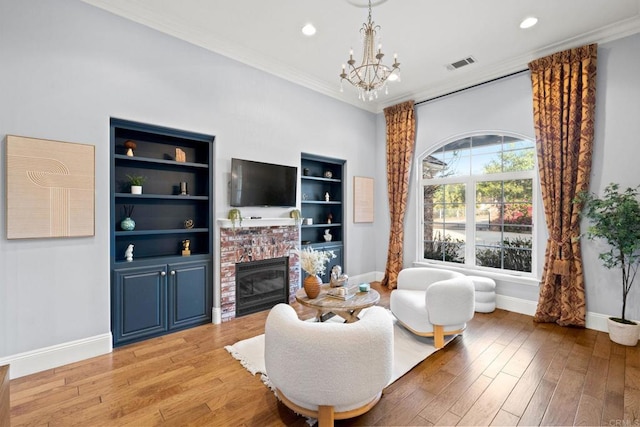 living room featuring an inviting chandelier, ornamental molding, a brick fireplace, and light hardwood / wood-style flooring