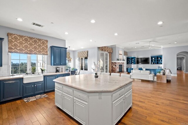 kitchen with blue cabinets, sink, white cabinets, a center island, and light wood-type flooring