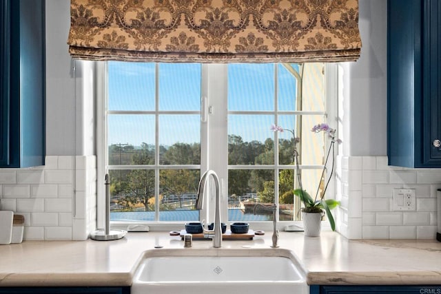 room details with tasteful backsplash, blue cabinets, light stone countertops, and sink