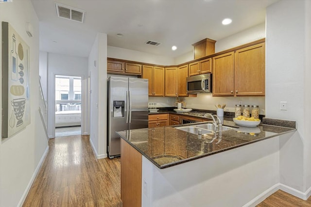 kitchen featuring stainless steel appliances, kitchen peninsula, sink, and dark stone countertops