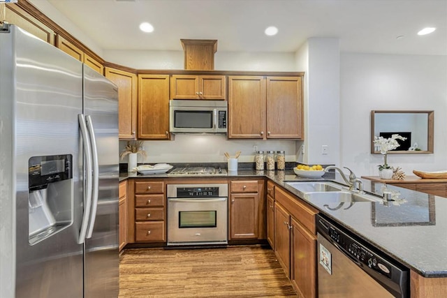 kitchen featuring appliances with stainless steel finishes, sink, light hardwood / wood-style flooring, and dark stone counters