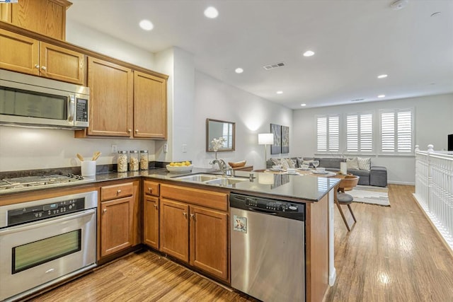 kitchen with appliances with stainless steel finishes, kitchen peninsula, sink, and light hardwood / wood-style flooring