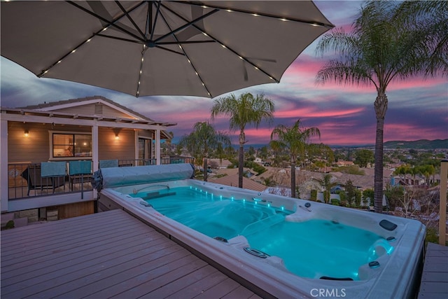 pool at dusk featuring a deck and a covered hot tub