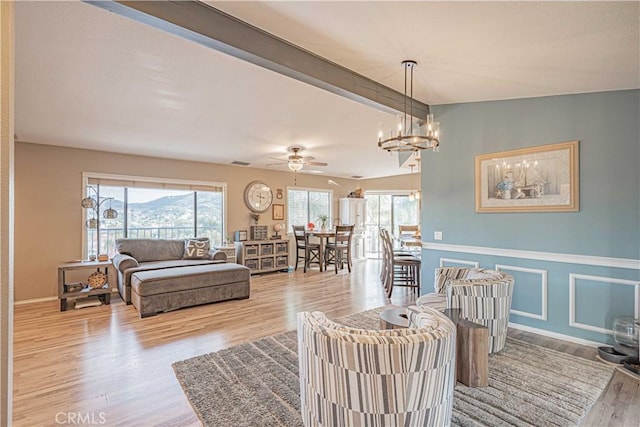 living room featuring lofted ceiling with beams, a mountain view, ceiling fan with notable chandelier, and light hardwood / wood-style flooring