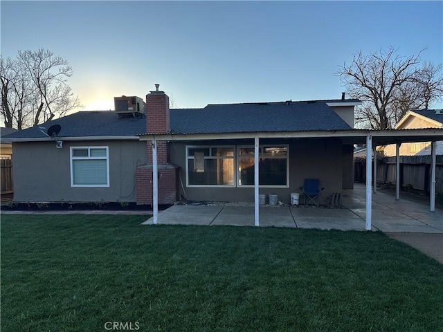 back house at dusk with a patio and a lawn