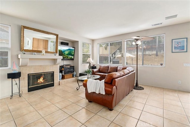 living area featuring light tile patterned flooring, ceiling fan, visible vents, and a tile fireplace