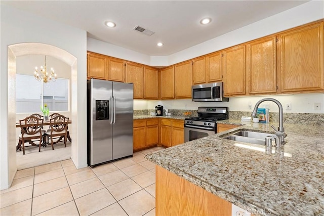 kitchen featuring visible vents, brown cabinetry, appliances with stainless steel finishes, light stone countertops, and a sink