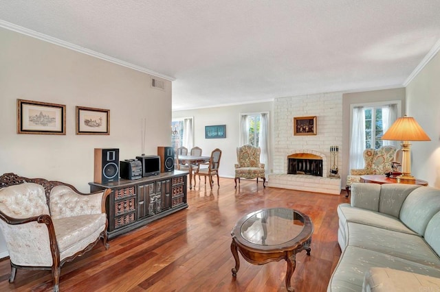 living room featuring a healthy amount of sunlight, wood-type flooring, a brick fireplace, and ornamental molding