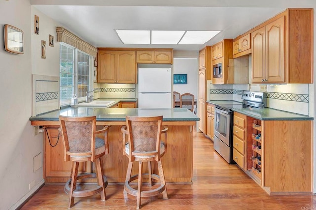 kitchen featuring sink, a kitchen breakfast bar, kitchen peninsula, stainless steel appliances, and light hardwood / wood-style flooring