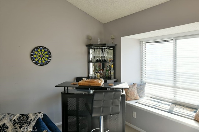 dining area with bar, vaulted ceiling, and a textured ceiling