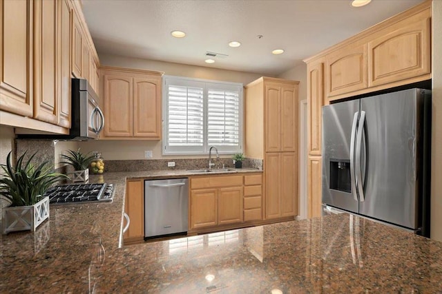 kitchen with appliances with stainless steel finishes, sink, light brown cabinets, and dark stone counters