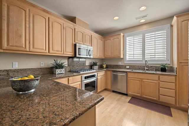 kitchen with light brown cabinetry, sink, dark stone countertops, light hardwood / wood-style floors, and stainless steel appliances