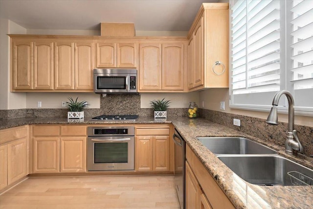 kitchen with stone counters, light brown cabinetry, sink, stainless steel appliances, and light hardwood / wood-style flooring