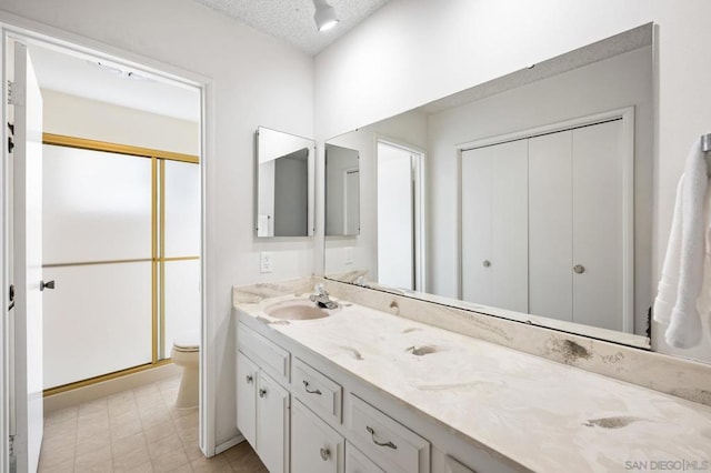 bathroom featuring vanity, toilet, a shower with shower door, and a textured ceiling