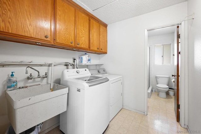 laundry room with cabinets, sink, a textured ceiling, and washing machine and clothes dryer