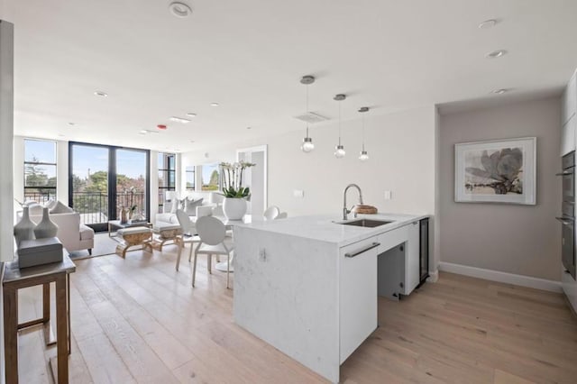 kitchen featuring hanging light fixtures, sink, white cabinets, and light wood-type flooring