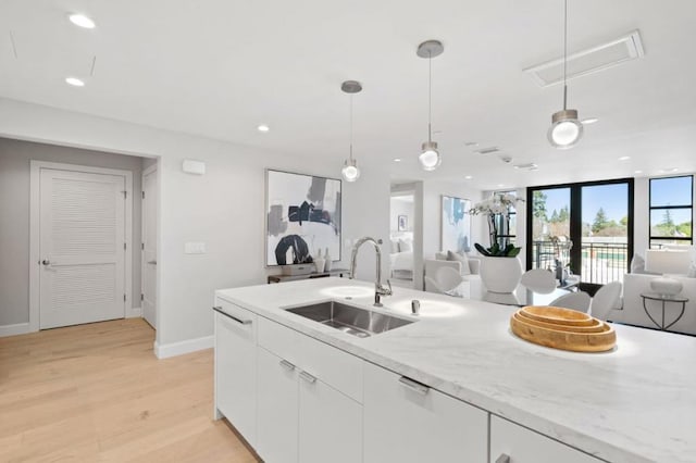 kitchen featuring sink, white cabinetry, light stone counters, light wood-type flooring, and pendant lighting