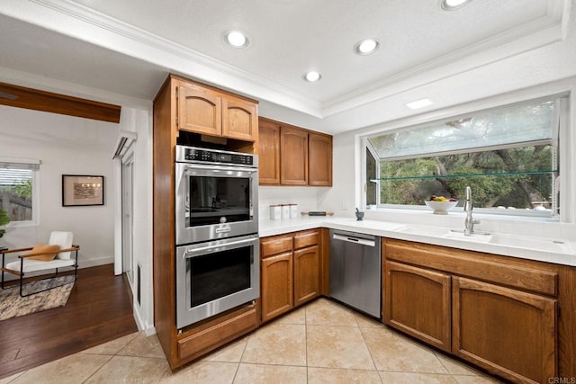 kitchen with appliances with stainless steel finishes, sink, ornamental molding, light tile patterned floors, and a raised ceiling