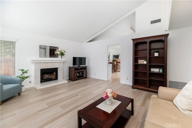 living room featuring a tiled fireplace, vaulted ceiling, and light wood-type flooring