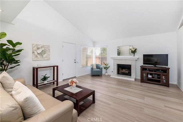 living room with a tiled fireplace, high vaulted ceiling, and light hardwood / wood-style flooring