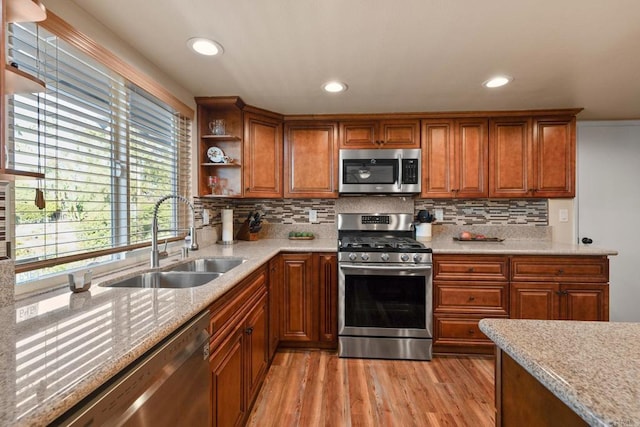 kitchen featuring sink, stainless steel appliances, tasteful backsplash, light stone countertops, and light wood-type flooring