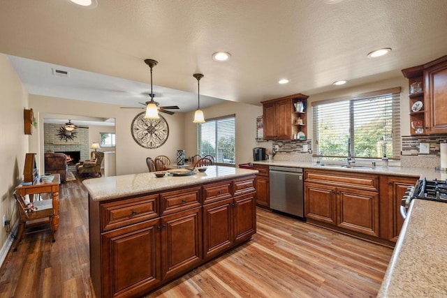 kitchen with sink, a brick fireplace, hardwood / wood-style flooring, pendant lighting, and stainless steel appliances