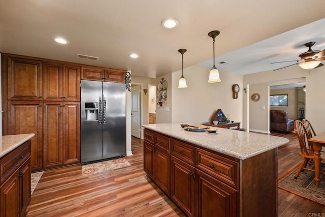 kitchen featuring decorative light fixtures, stainless steel fridge, light stone countertops, and wood-type flooring