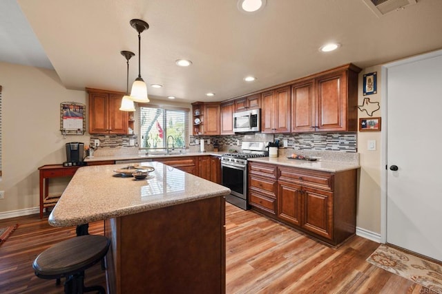 kitchen featuring pendant lighting, sink, stainless steel appliances, a center island, and light hardwood / wood-style floors