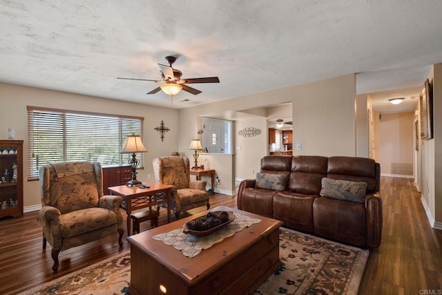 living room with a textured ceiling, dark wood-type flooring, and ceiling fan