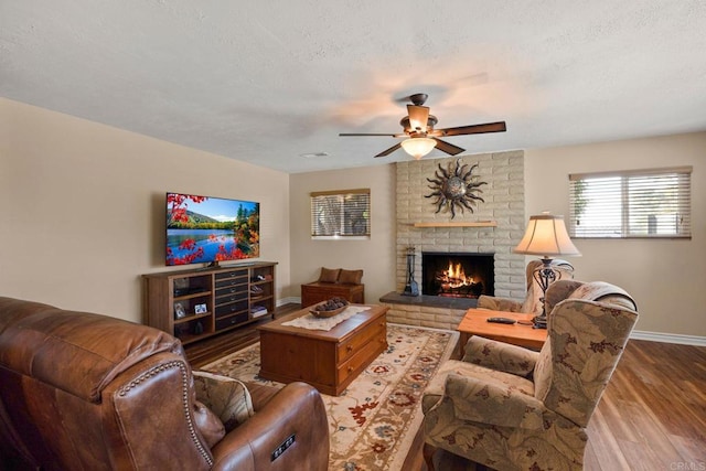 living room with ceiling fan, light wood-type flooring, a textured ceiling, and a fireplace