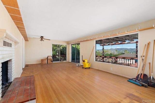 unfurnished living room featuring hardwood / wood-style flooring, ceiling fan, a fireplace, and a mountain view