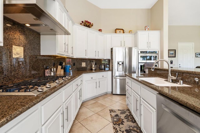 kitchen featuring wall chimney exhaust hood, sink, dark stone countertops, appliances with stainless steel finishes, and white cabinets