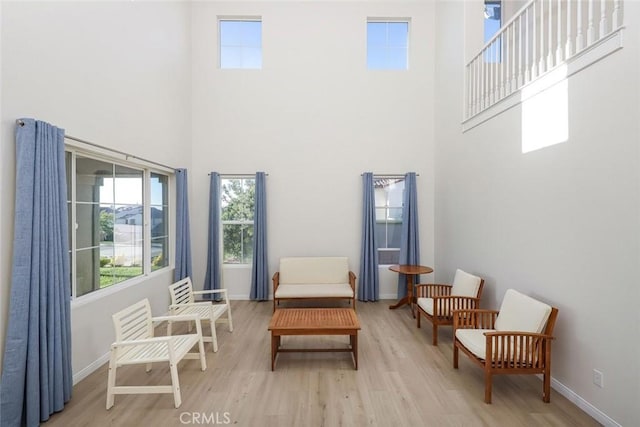 sitting room featuring a towering ceiling, light wood-style flooring, and baseboards