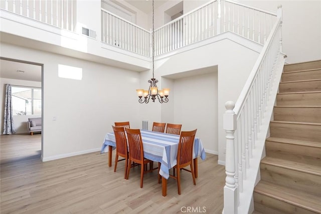 dining area featuring a chandelier, visible vents, a high ceiling, and wood finished floors