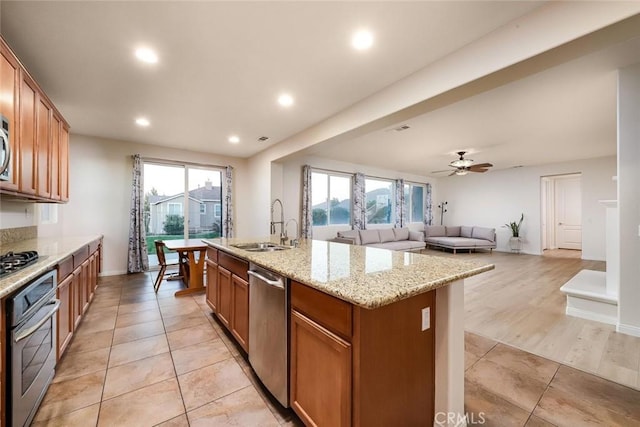 kitchen featuring a center island with sink, brown cabinetry, appliances with stainless steel finishes, a healthy amount of sunlight, and a sink