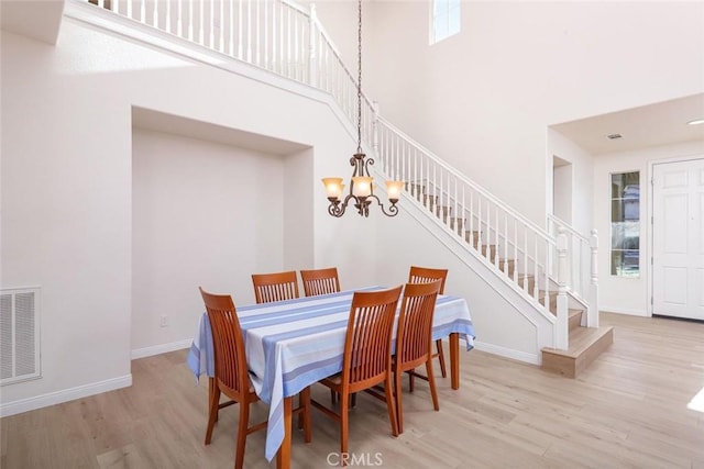 dining area featuring baseboards, visible vents, a towering ceiling, stairway, and wood finished floors