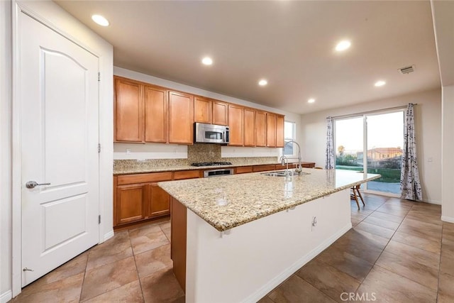 kitchen with recessed lighting, appliances with stainless steel finishes, a sink, an island with sink, and light stone countertops